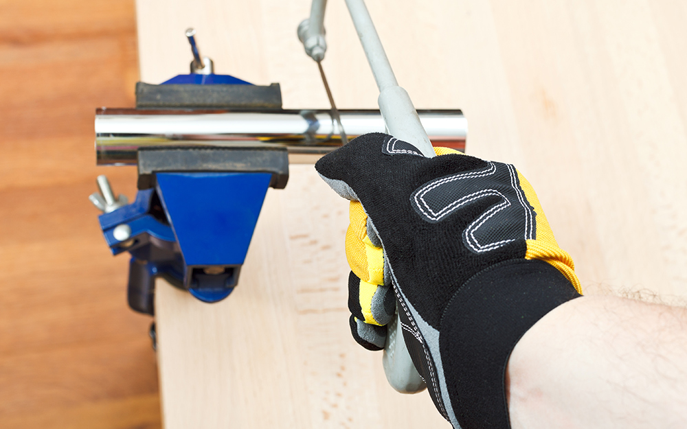A person uses a hacksaw and vise to cut galvanized steel pipe.