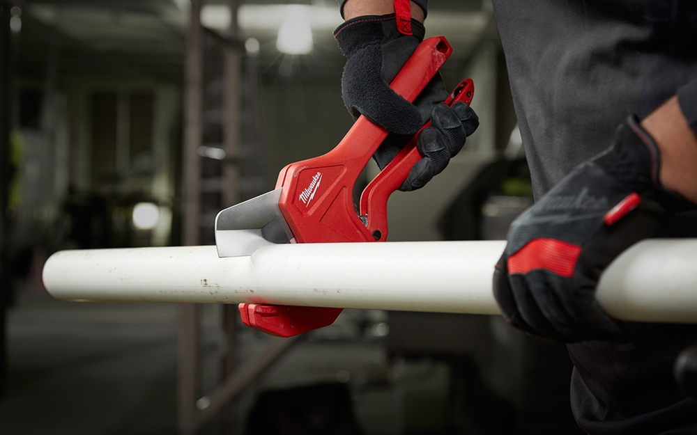 A person cutting PVC pipe with a ratchet-style cutter.