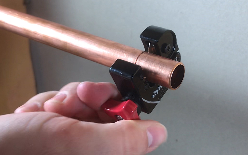 A person using a copper tubing cutter on a length of tubing.